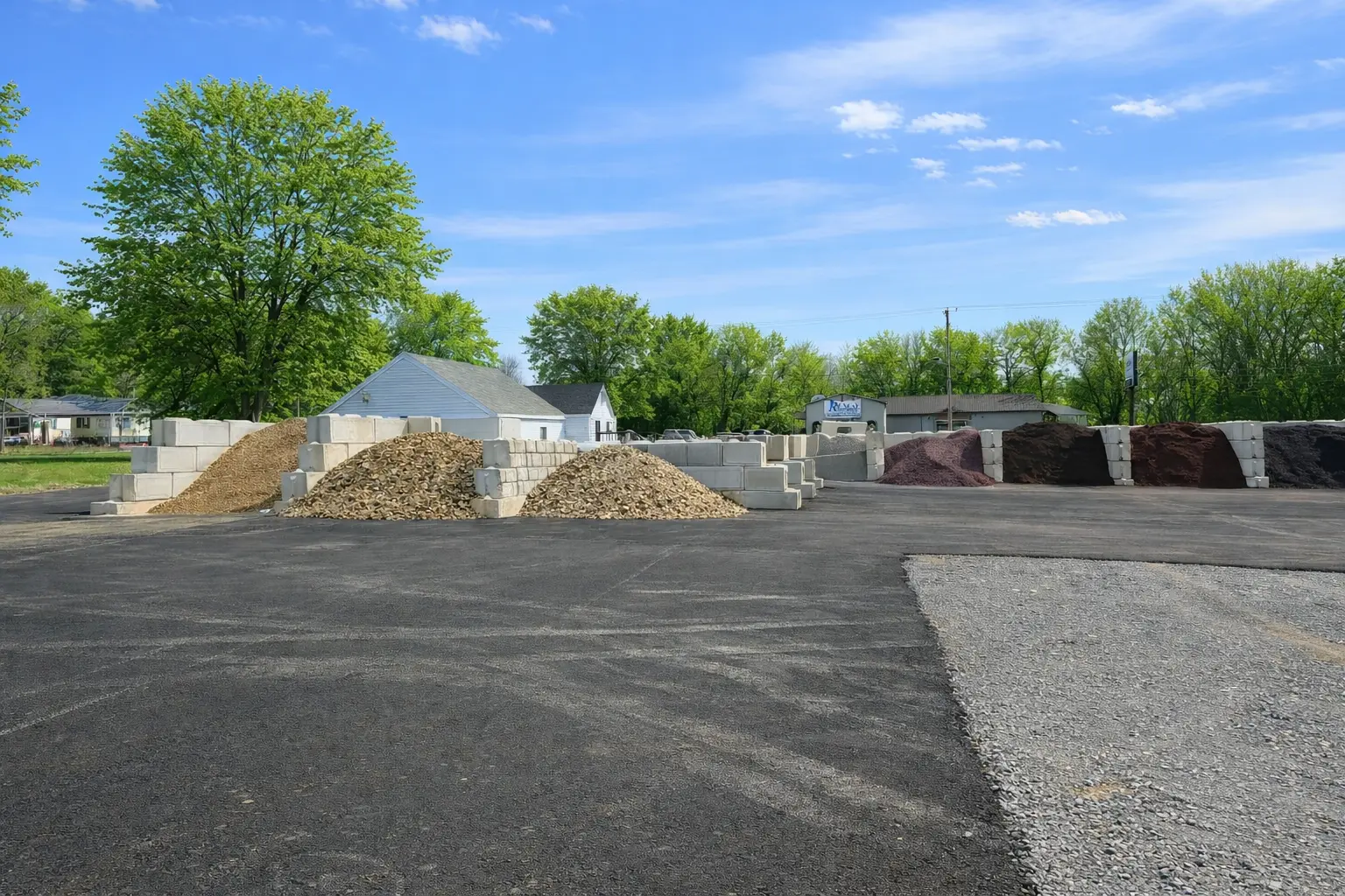 Wide view of JTR Garden Center bulk materials yard with decorative stone gravel and mulch piles under blue sky