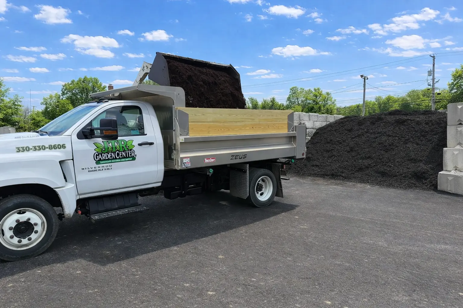 JTR Garden Center delivery truck loading bulk mulch at landscape supply yard on sunny day with blue skies